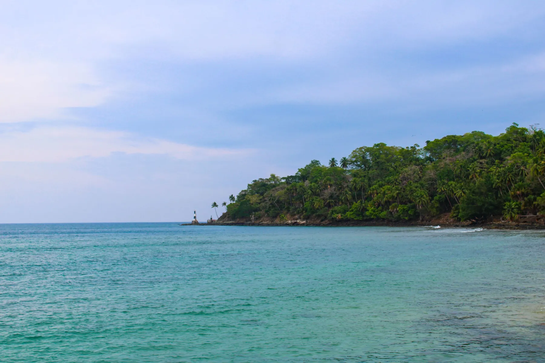 Serene tropical coastline with lighthouse and lush greenery in Andaman, India.
