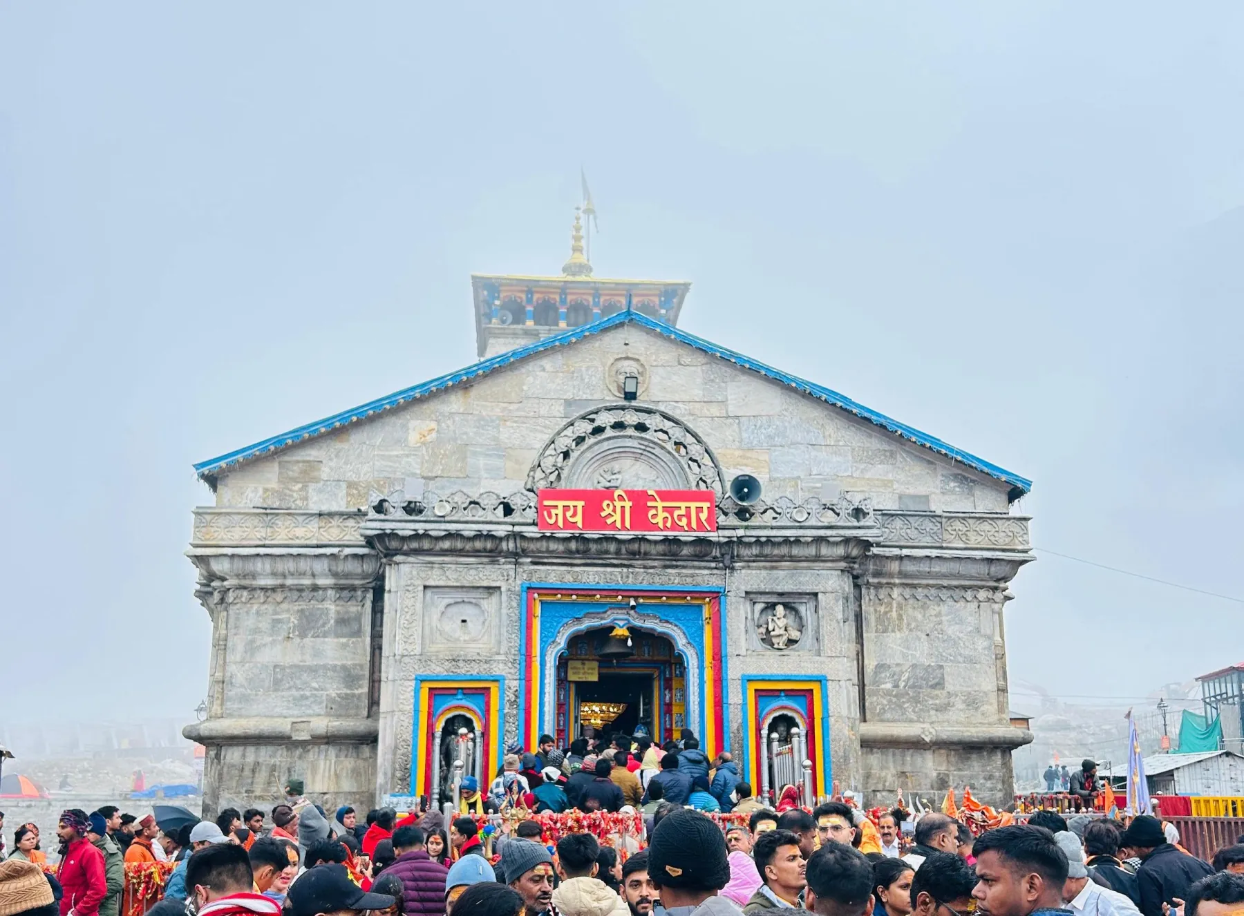 A large crowd gathers at the historic Kedarnath Temple in India amidst misty weather.
