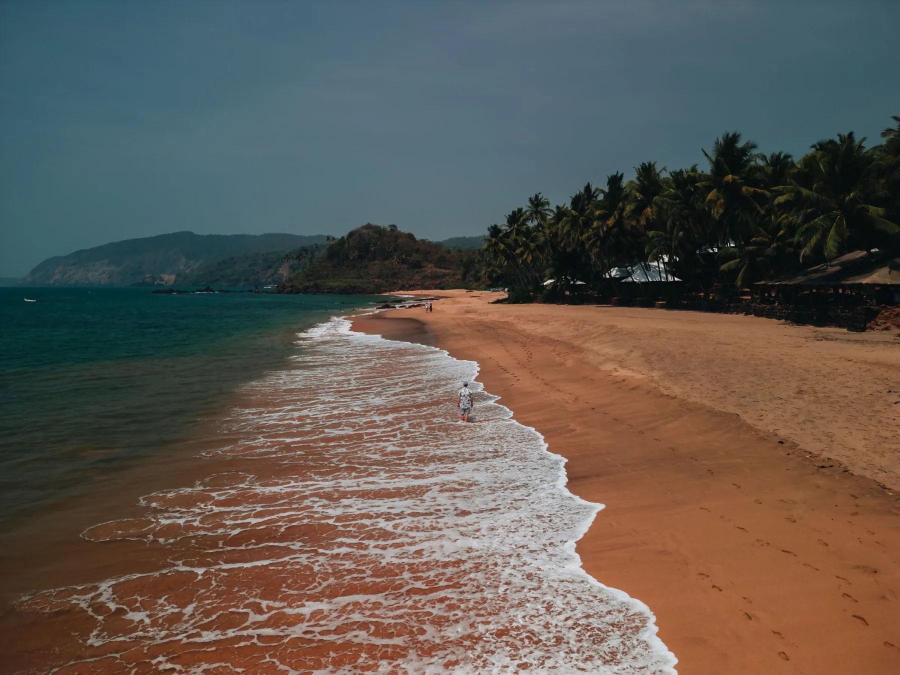 A picturesque aerial view of a serene beach in Goa with golden sands and gentle waves during sunset.