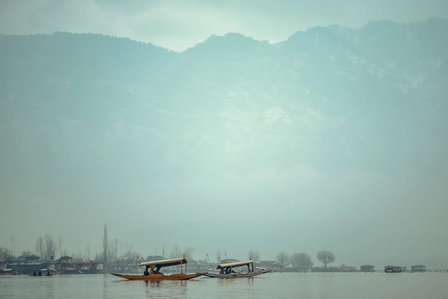 Two traditional shikara boats on a serene misty lake with distant mountains.
