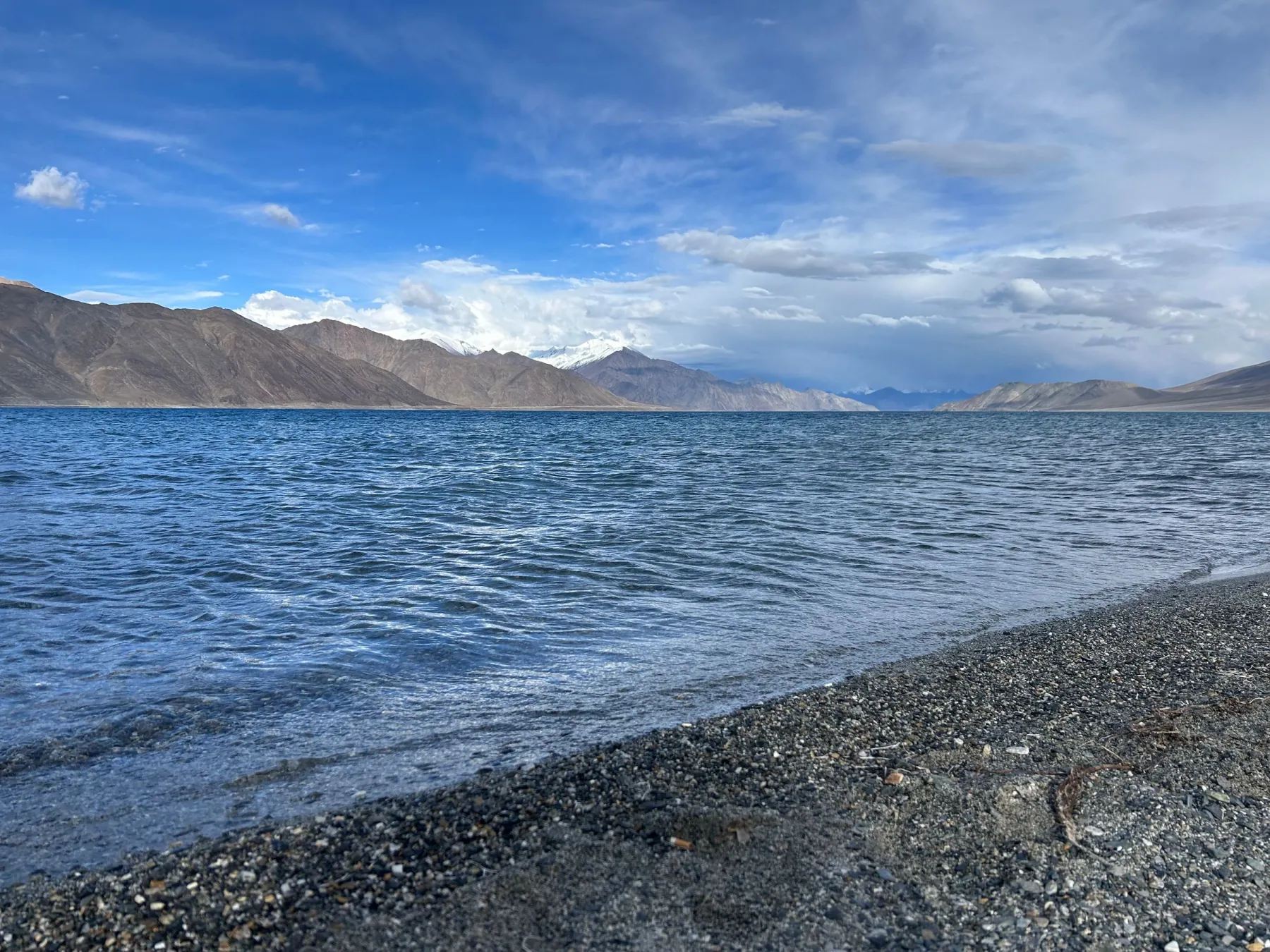 Vivid image of Pangong Lake with majestic mountains under a blue sky. Ideal for nature and travel enthusiasts.