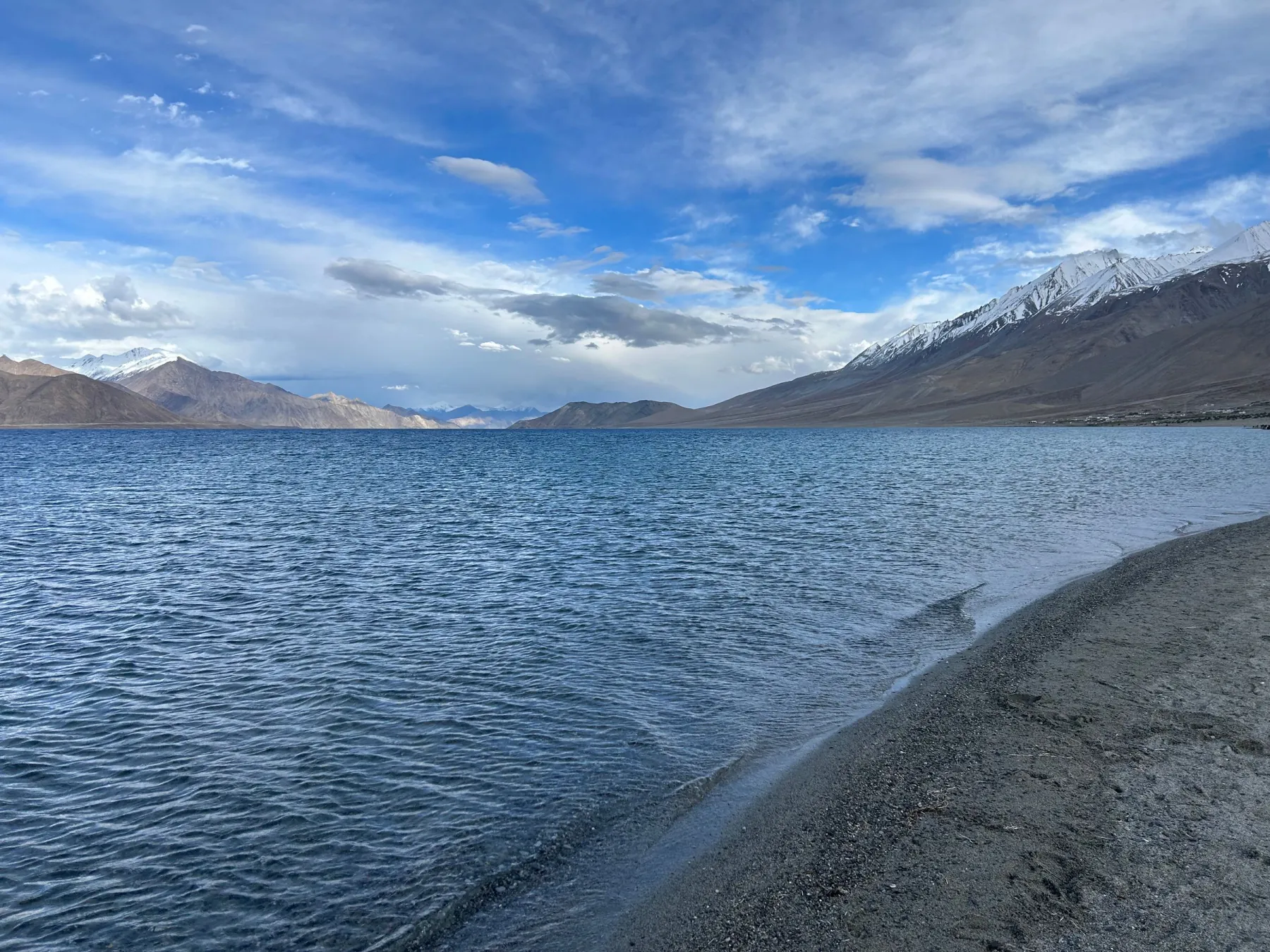 Breathtaking view of Pangong Tso Lake with mountain backdrop under a vibrant sky.