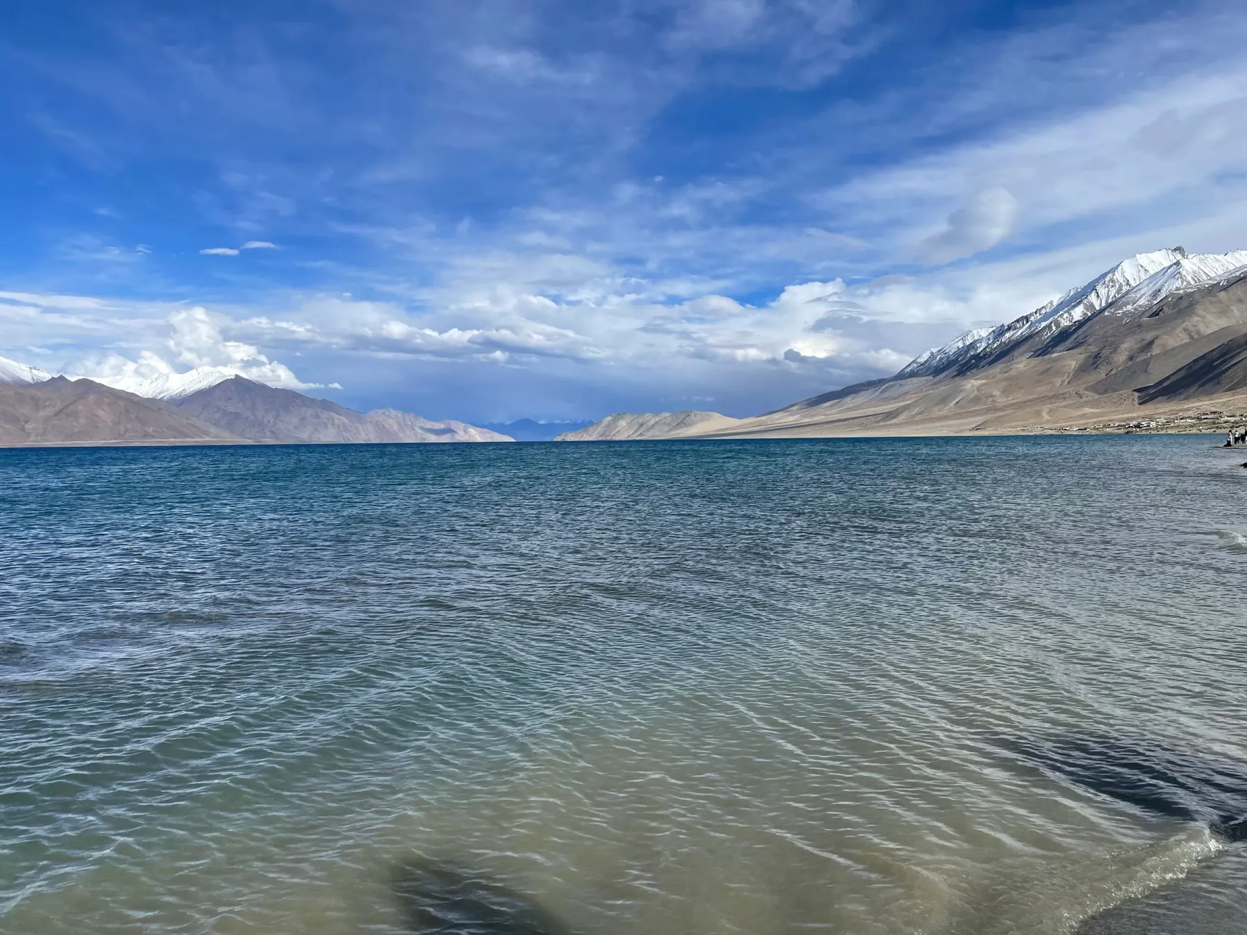 Breathtaking view of Pangong Lake with snow-capped mountains under a vibrant blue sky.