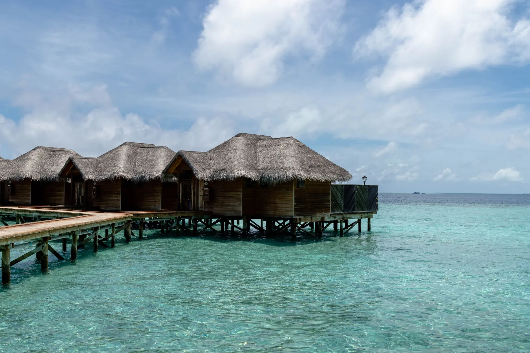 Overwater bungalows with thatched roofs on a turquoise ocean, under a clear blue sky in the Maldives.