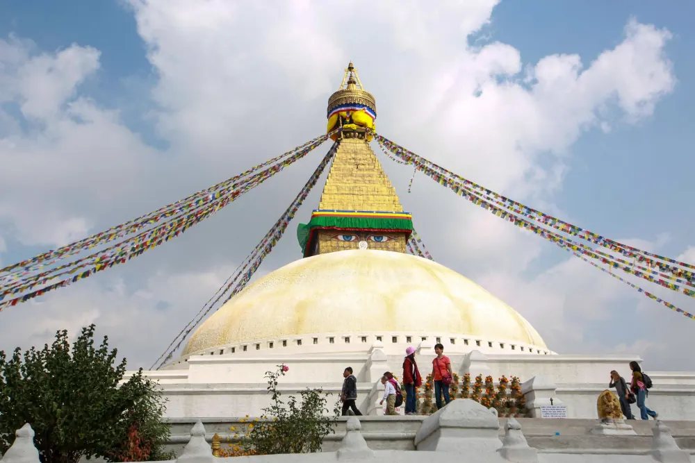 View of Boudhanath Stupa with prayer flags in Kathmandu, Nepal under a bright sky.