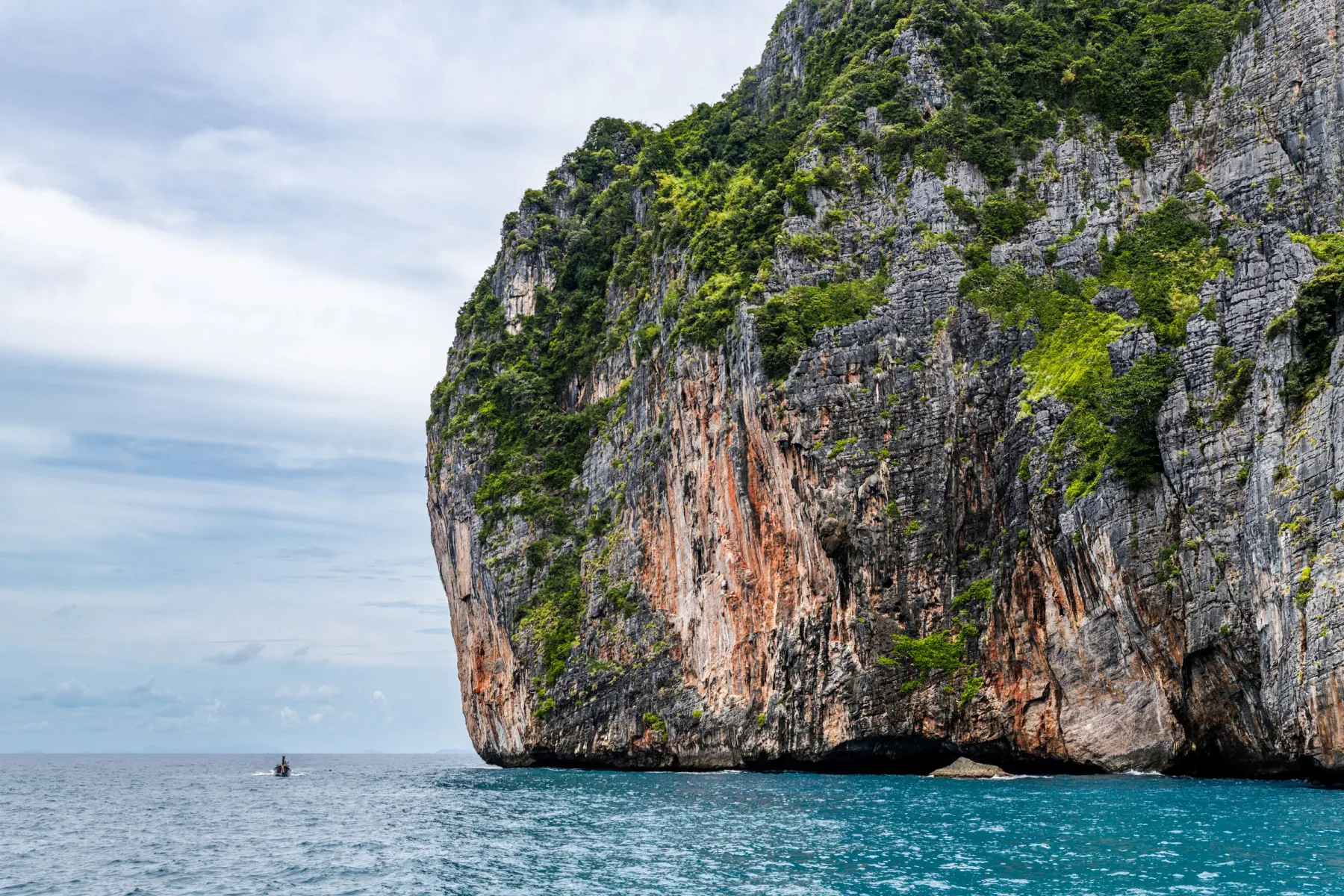 Majestic cliff rising from turquoise sea under a clear sky in Phuket, Thailand.